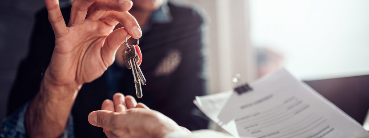 Real estate agent sitting at the desk by the window and passing keys to his client in the office