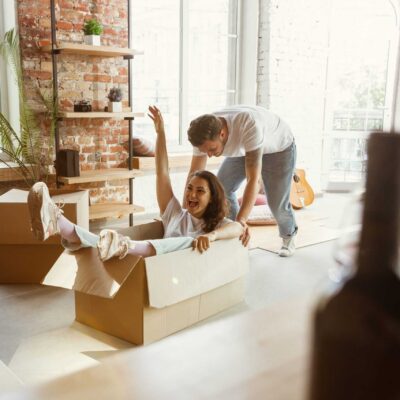 Young couple moved to a new house or apartment. Having fun with cardboard boxes, relaxing after cleaning and unpacking at moved day. Look happy. Family, moving, relations, first home concept.