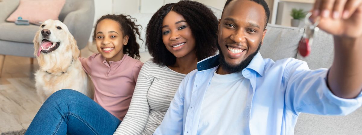 Moving Day. Happy African American family of three people and a dog holding and showing keys of their new apartment house. Excited black homeowners enjoying celebrating relocation