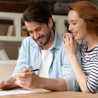 Overjoyed young Caucasian couple clients sign paper document make agreement buy first shared house together. Happy man and woman spouses feel excited close deal rent home or take bank loan.