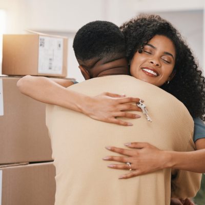 Happy couple, hug and real estate in new home, moving in or boxes for investment or ownership together. Man and woman with keys in embrace for property, relocation or renovation in house mortgage.